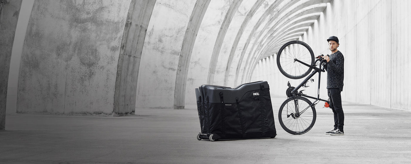 EVOC Bike Travel Bag next to man holding bike upright homepage slider