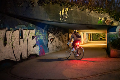 Bike commuter wearing EVOC backpack using bicycle lights riding at night heading into a tunnel
