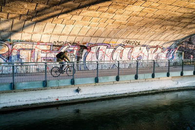 Man wearing an EVOC backpack bike commuting along bike path under a bridge