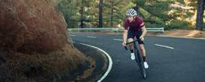 EVOC athlete cycling up a black asphalt mountain road with pine trees in the background