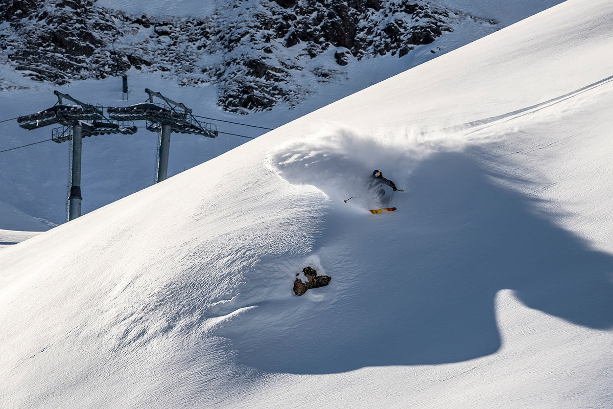 EVOC athlete skiing powder snow with ski lift in the background